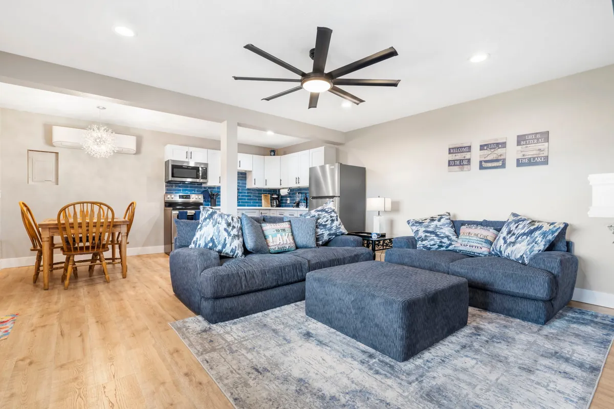 A spacious living area featuring a large sectional sofa adorned with blue accent pillows, a dining table ready for shared meals or games, and an open kitchen just beyond. The scene exudes warmth and comfort, designed for group enjoyment.