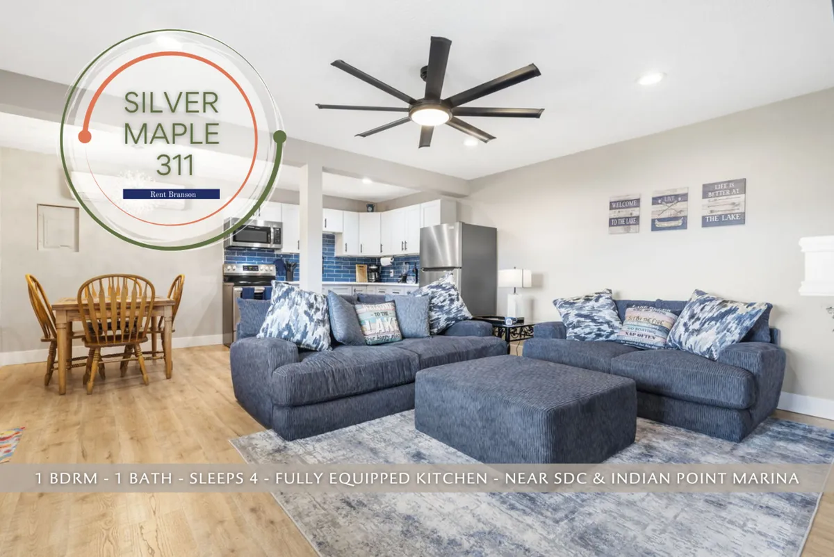 A spacious and modern living area featuring a large sectional sofa ideal for group relaxation, a dining table set for shared meals or games, and an open kitchen area visible in the background. The layout is open and inviting, with ample natural light and sleek finishes that enhance the contemporary comfort of the space.