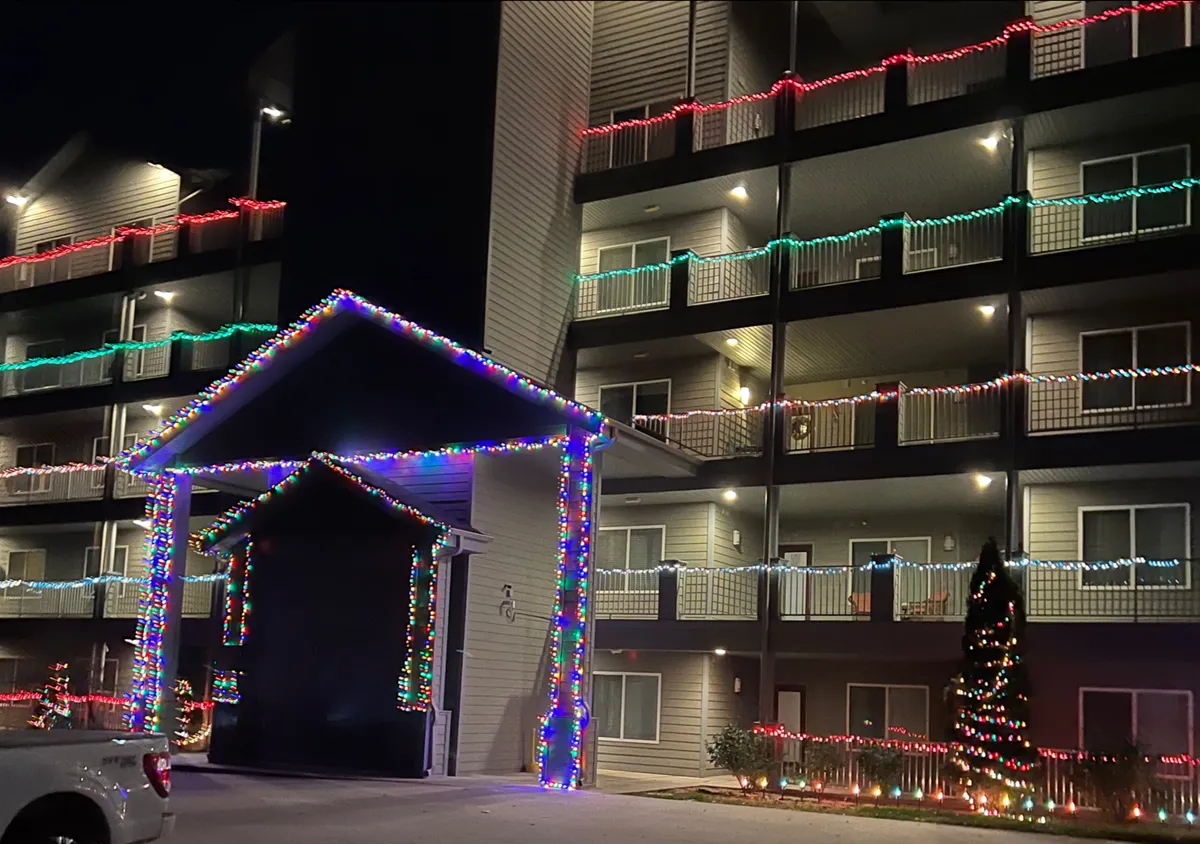 An exterior view featuring festive decorative lights, a well-lit building entrance, and a sparkling Christmas tree. The scene is lively, capturing the joyful atmosphere of holiday gatherings and seasonal celebrations.