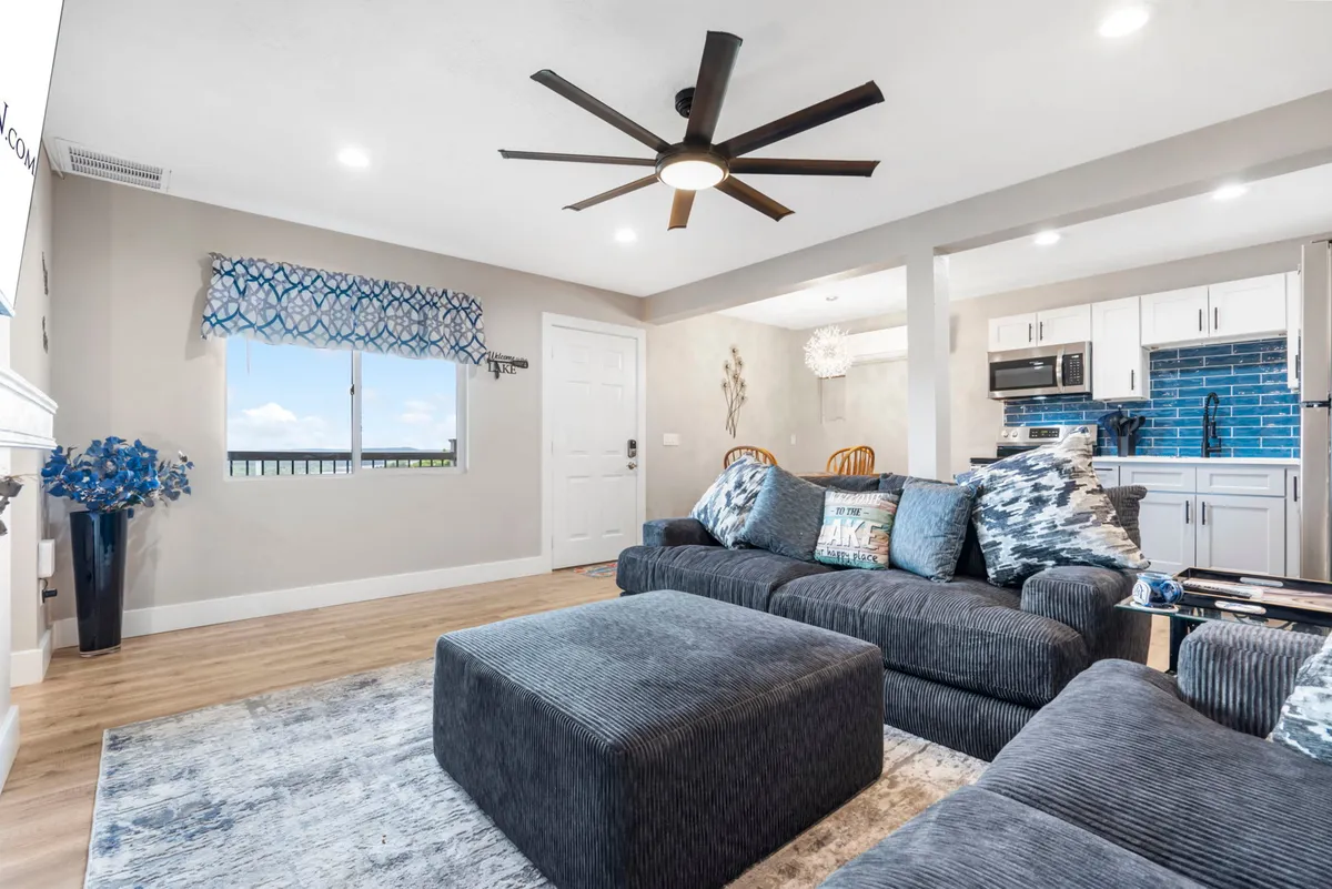 A comfortable, inviting living area inside the condo, featuring a sofa, ceiling fan, rug, and a large window with a scenic view. The natural light and view through the window connect the interior with the outdoors, suggesting cozy moments after active days.