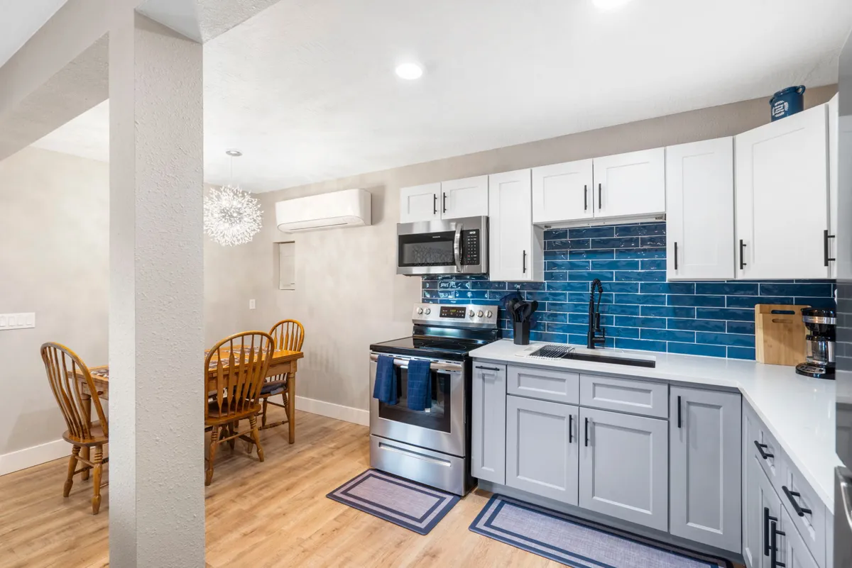 A warm, inviting dining area adjacent to the kitchen, featuring a blue backsplash, dining table, and stainless steel appliances in the background. The scene suggests family gatherings and social dining, with the blue tile carrying through the cohesive kitchen-dining space.