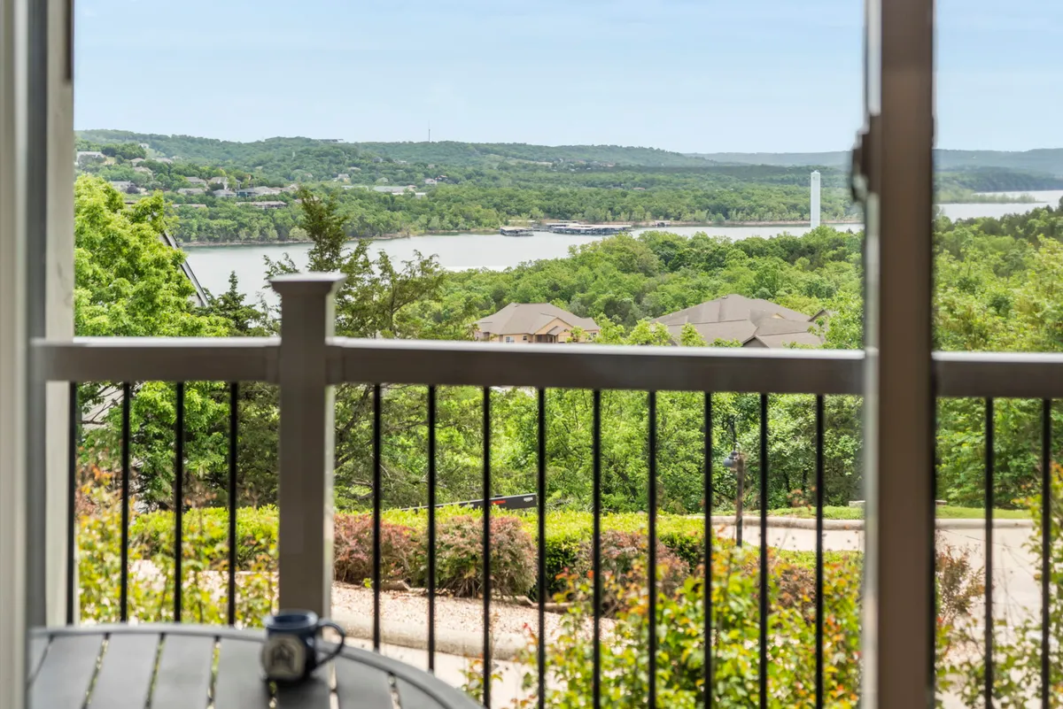 A tranquil balcony overlooking Table Rock Lake with a clear view of the water through the railing, surrounded by lush greenery. The setting is perfect for sipping coffee or enjoying a book while taking in the lake panorama.