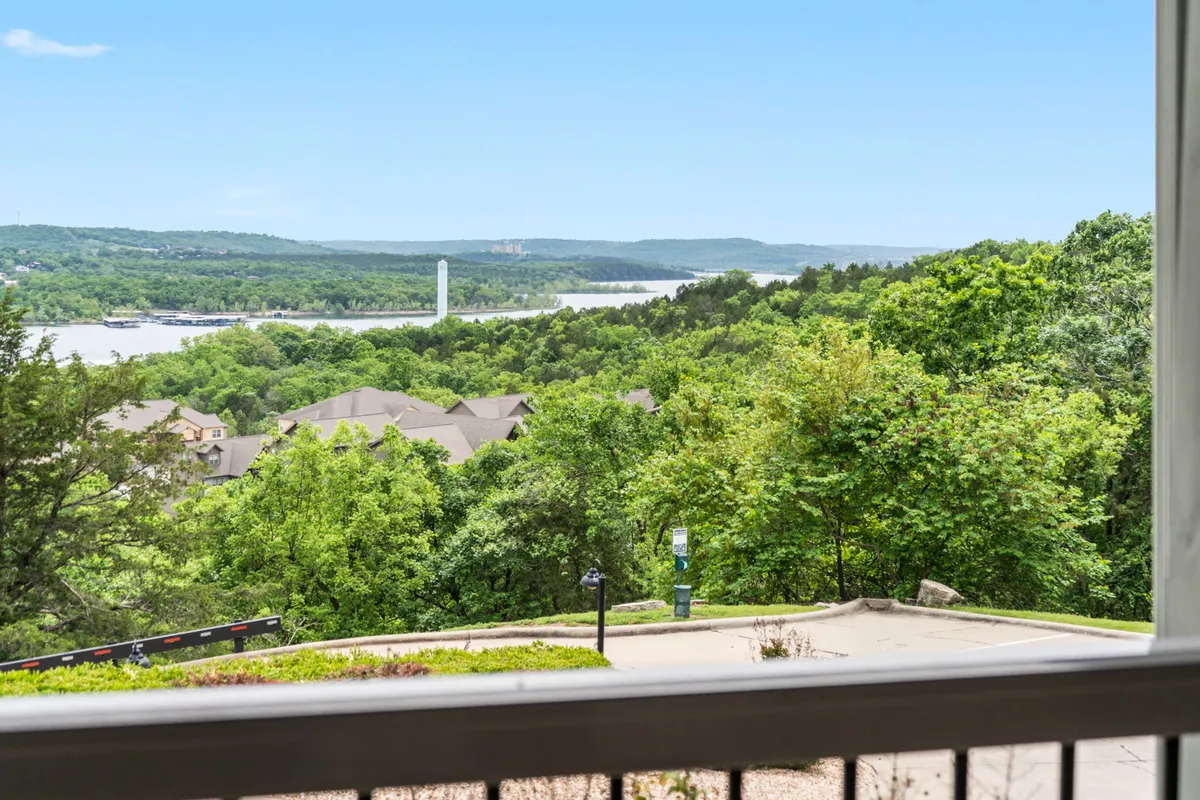 The image presents a scenic view of lush greenery, a river, distant hills, and residential rooftops, highlighting the natural surroundings that can be enjoyed from the property’s patio or nearby walkways. It conveys the peaceful, budget-friendly appeal of the location.