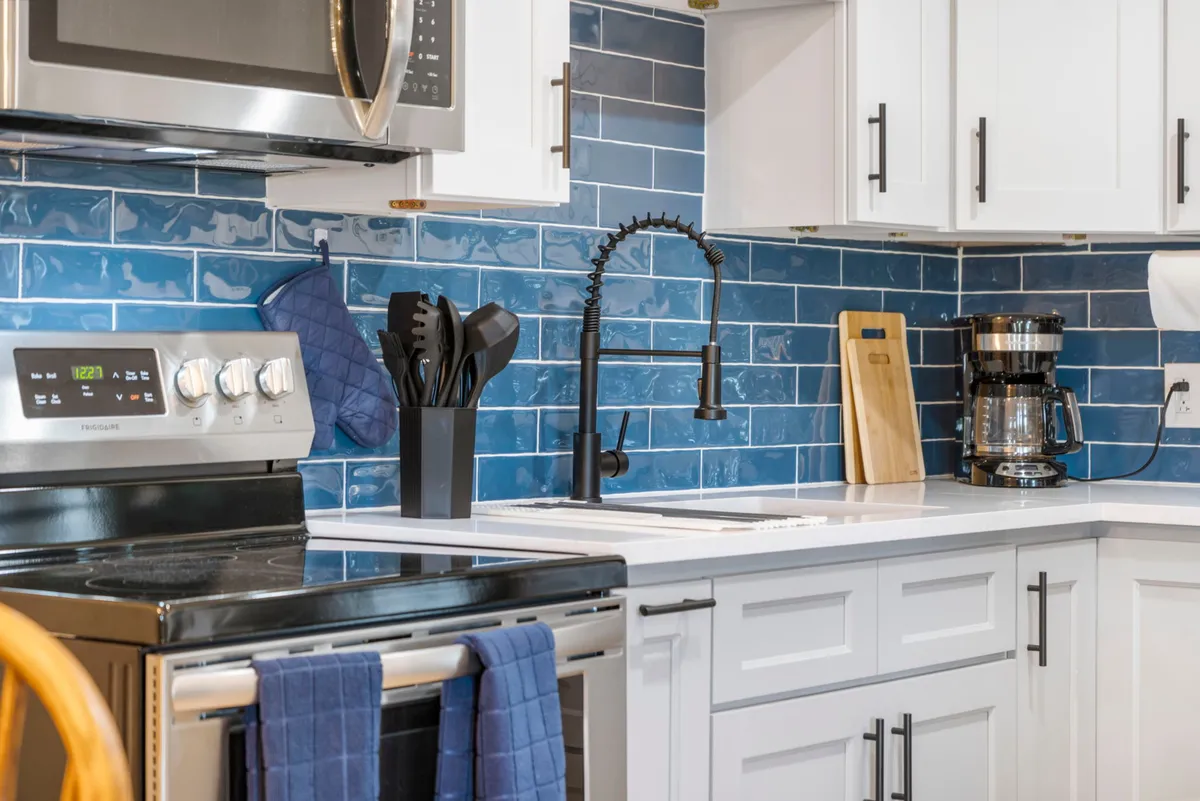 A closer, modern view of the kitchen area focusing on the blue subway backsplash, stainless steel appliances, a sleek black faucet, and a coffee maker. The image conveys a cozy yet contemporary vibe, perfect for everything from brewing morning coffee to preparing special meals.