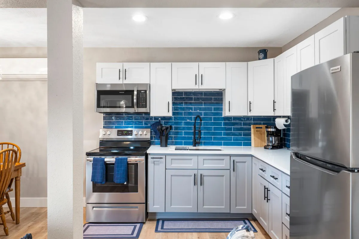This image presents a welcoming kitchen with a striking blue backsplash, stainless steel appliances, and crisp white cabinetry. The space is clearly designed for both cooking and socializing, and the blue tile is a major visual focal point, catching the eye and setting a lively modern tone.