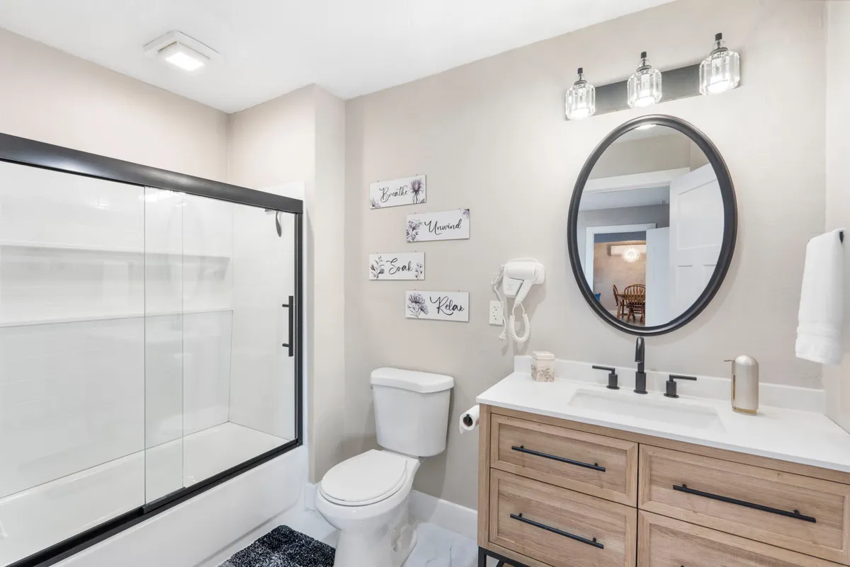 A bright ensuite bathroom with a framed mirror, wooden vanity, and a glass shower enclosure. The space feels airy and inviting, perfect for unwinding after a long day.
