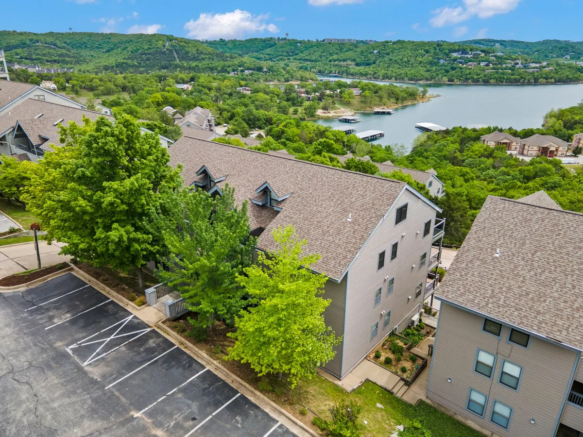 An exterior shot featuring green trees, a picturesque lake view, and nearby buildings, emphasizing the proximity to outdoor recreation and beautiful natural surroundings. The parking area suggests easy access for group arrivals.