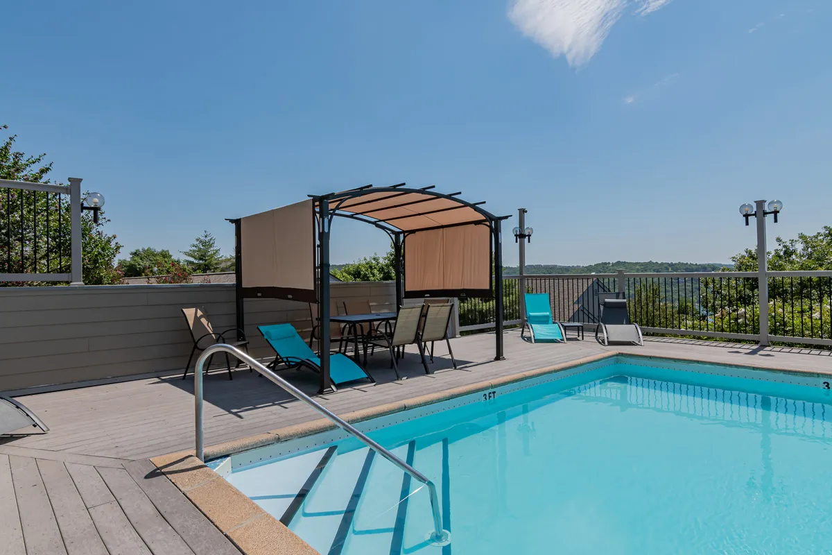 A sparkling outdoor swimming pool surrounded by lounge chairs and a shaded canopy area, set amid a landscaped backdrop. The pool area radiates a peaceful, resort-like ambiance, inviting both relaxation and socializing.